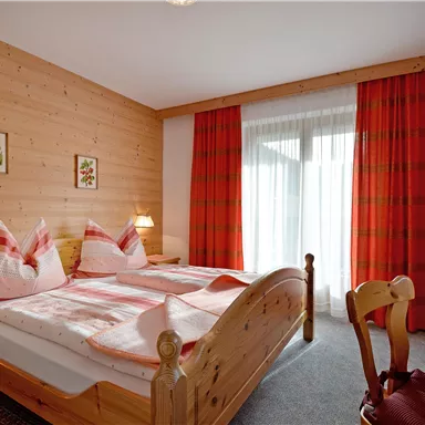 Ein gemütliches Schlafzimmer mit zwei Einzelbetten und Holzverkleidung. Die warmen Farben und großen Fenster sorgen für eine einladende Atmosphäre.