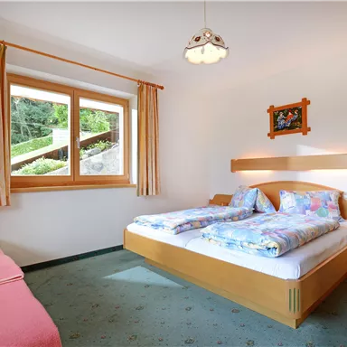 Ein helles Zimmer mit zwei Betten und einem gemütlichen Sofa. Große Fenster bieten Blick auf die Natur.