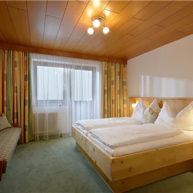 Ein gemütliches Schlafzimmer mit zwei Betten und Holzpaneelen. Der Raum hat große Fenster und farbenfrohe Gardinen.