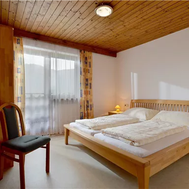 Ein gemütliches Schlafzimmer mit einem Doppelbett und Holzdecke. Der Raum ist hell und modern eingerichtet, mit einer kleinen Sitzecke.