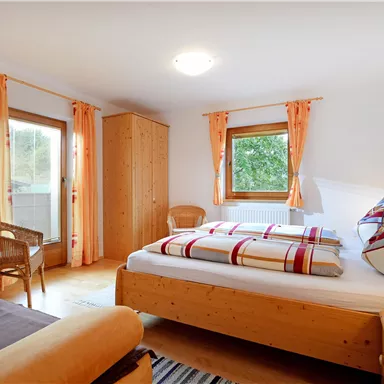 A cozy bedroom with a large bed, bright curtains, and wooden furniture. There is a desk and a television in the corner.