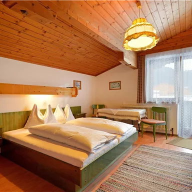 Ein gemütliches Schlafzimmer mit Holzdecke und zwei Betten. Außerdem gibt es einen kleinen Balkon und eine warme Beleuchtung.