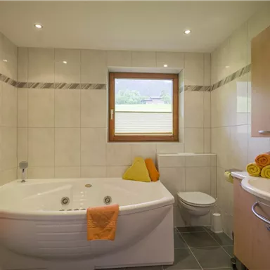 A modern bathroom with a whirlpool tub and a shower. There are large windows and colorful towels on the sink.