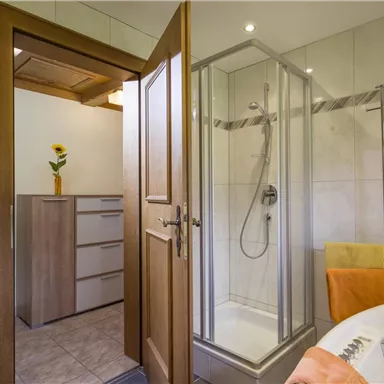 A modern bathroom with a shower and a bathtub. The walls are tiled in light colors, and a small bouquet of flowers is on the shelf.