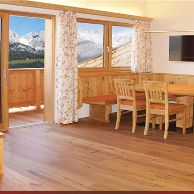 Ein modernes Wohnzimmer mit Holzmöbeln und einem Essbereich. Große Fenster bieten einen Blick auf die Berge.