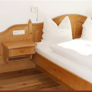 Ein gemütliches Zimmer mit einem Doppelbett und hellen Holzmöbeln. Ein Tisch mit einer Obstschale ergänzt die freundliche Atmosphäre.