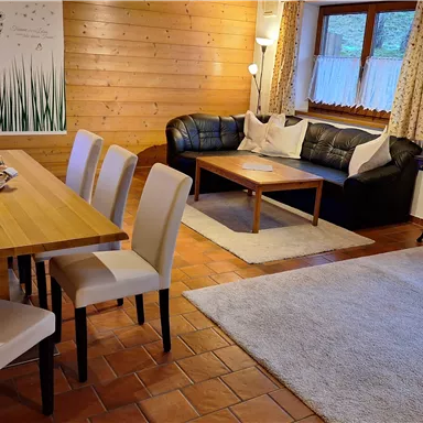 A cozy living room with a dining table and chairs. In the background, a sofa and decorations can be seen.