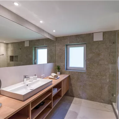 A modern bathroom with bright walls and a large mirror. The furnishings are made of wood and offer plenty of storage space.