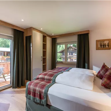 A cozy hotel room with two beds, a desk, and a view of the terrace. Plenty of natural light and appealing amenities create a relaxing atmosphere.