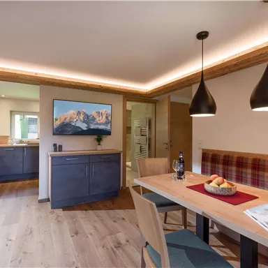 A modern, bright apartment with a dining area and a kitchenette. The space has a cozy atmosphere with wooden details and stylish lamps.