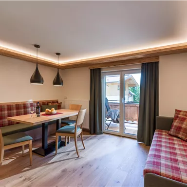 A modern living room with a dining table and chairs. Large windows provide access to a balcony and plenty of daylight.