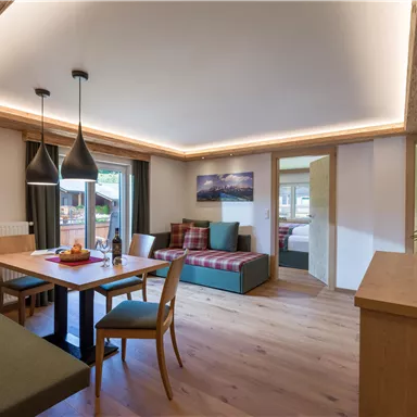 A stylishly furnished living kitchen with a dining table and modern lighting elements. The room features light wood and large windows for plenty of daylight.