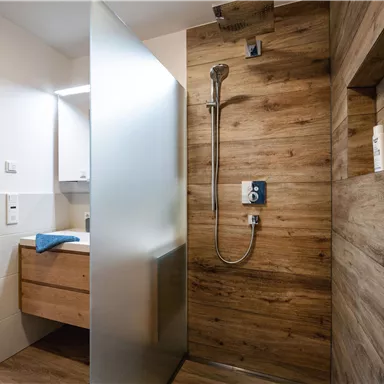 Ein modernes Badezimmer mit einer Dusche aus Holzoptik. Es gibt einen Waschbecken-Unterschrank und eine frosted Glasscheibe.