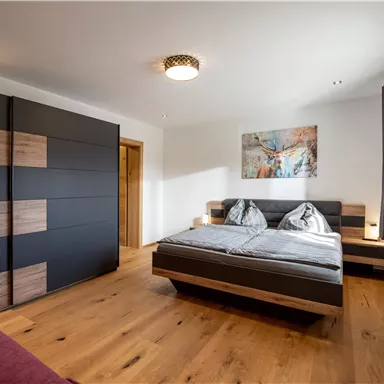 Ein modernes Schlafzimmer mit einem Doppelbett und Holzfußboden. Die Wände sind hell, und es gibt ein Gemälde über dem Bett.