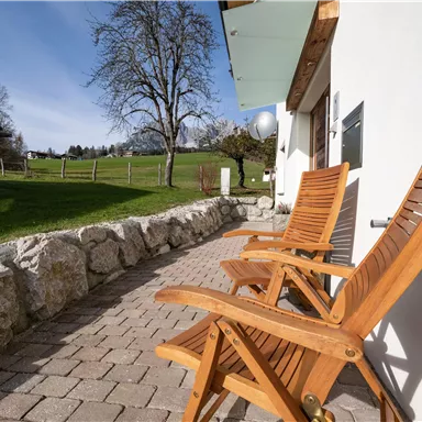 Eine gemütliche Terrasse mit zwei Holzstühlen und Sicht auf eine grüne Wiese. Der Himmel ist klar und die Umgebung ist ruhig.