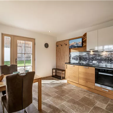 Eine moderne Küche mit Holzdetails und einem Essbereich. Große Fenster lassen viel Licht herein und bieten einen Blick auf den Außenbereich.