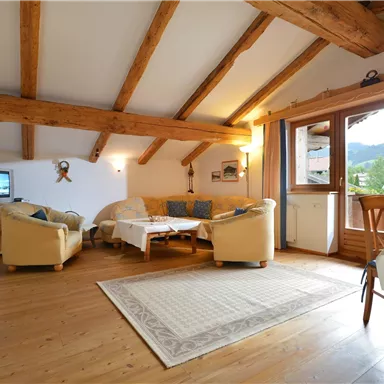 Ein gemütliches Wohnzimmer mit Holzdecken und großen Fenstern. Das Zimmer ist hell und einladend, mit einem Sofa und einem Tisch.