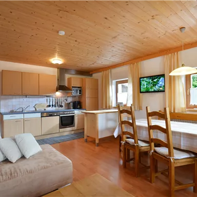 Eine gemütliche Küche mit Holzdekor und einem Esstisch. Der Raum ist hell und freundlich, mit Fenstern und modernen Küchengeräten.