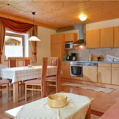 Eine helle Küche mit Holzregalen und einem Esstisch. Moderne Geräte und gemütliche Möbel schaffen eine einladende Atmosphäre.