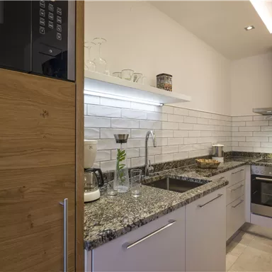 Eine moderne Küche mit Granitoberflächen und weißen Fliesen. Sie ist gut ausgestattet mit Geräten und bietet viel Licht.