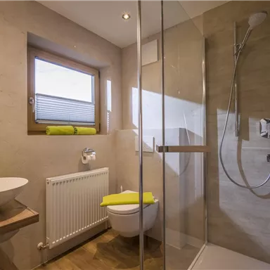A modern bathroom with a glass shower and a simple sink. Bright walls and a window create a bright, inviting atmosphere.