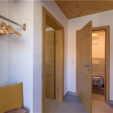 Ein heller Flur mit hölzernen Türen und einem Stuhl. Im Hintergrund ist ein Badezimmer sichtbar.