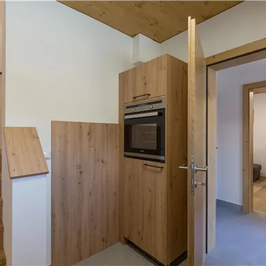 Eine moderne Küche mit einem Holzschrank und einem eingebauten Ofen. Im Hintergrund sind Treppen und ein weiteres Zimmer sichtbar.