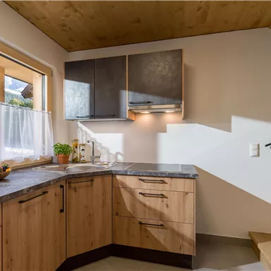 Eine moderne Küche mit Holzschränken und einer eleganten Arbeitsfläche. Das Licht strömt durch die Fenster und schafft eine einladende Atmosphäre.