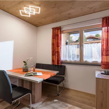 Ein gemütlicher Essbereich mit einem Tisch und vier Stühlen. Große Fenster lassen viel Tageslicht herein und die Wände sind in hellen Tönen gehalten.