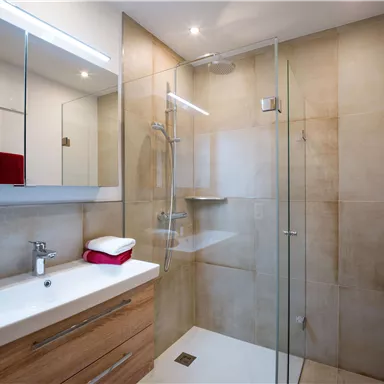 Ein modernes Badezimmer mit einer Glasdusche und einer hellen, neutralen Farbpalette. Holzdetails und spiegelnde Oberflächen schaffen eine einladende Atmosphäre.