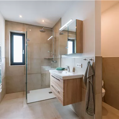 Ein modernes Badezimmer mit einer großzügigen Dusche und Holzwaschtisch. Helle Farben und viel Tageslicht schaffen eine einladende Atmosphäre.