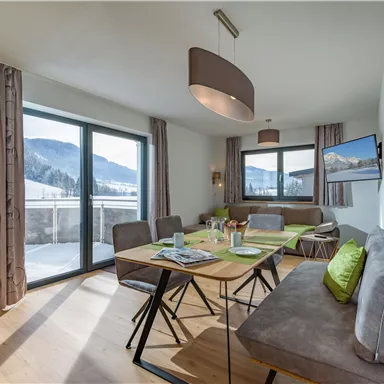 Ein modernes Wohnzimmer mit großen Fenstern und Blick auf die Berge. Der Raum ist elegant eingerichtet mit einem Esstisch und bequemen Sitzgelegenheiten.