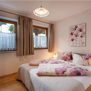 Ein gemütliches Schlafzimmer mit einem Doppelbett und hellen Wänden. Große Fenster und eine Blumenmalerei sorgen für eine einladende Atmosphäre.