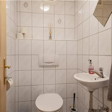 Ein kleines, sauberes Badezimmer mit weißen Fliesen. Es enthält eine Toilette, ein Waschbecken und einen Handtuchhalter.