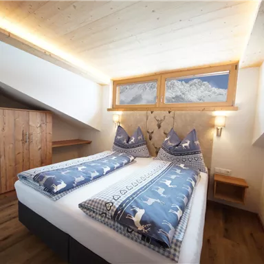 Ein gemütliches Schlafzimmer mit zwei Betten und traditionellen Kissen. Der Raum hat Holzverkleidung und große Fenster mit Blick auf die Berge.