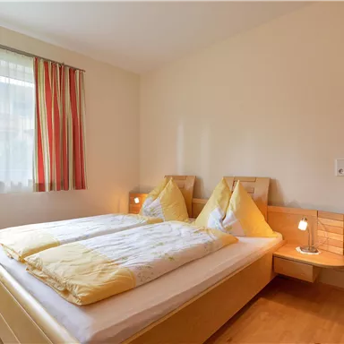 A bright bedroom with a double bed and yellow bedcovers. Large windows provide plenty of daylight and an inviting atmosphere.