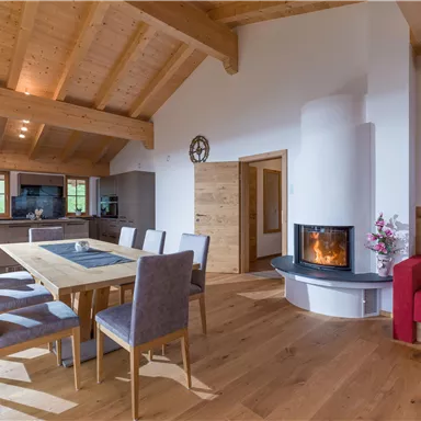 A modern living and dining room with a wood ceiling. A large table and a cozy fireplace create an inviting atmosphere.
