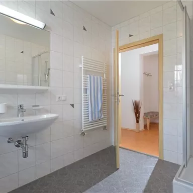 A modern bathroom with bright tiles and a shower. There is a sink, a towel holder, and an open access to another room.