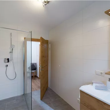 A modern bathroom with a glass shower and a wooden sink. The walls are designed in light colors, and a door leads to another room.