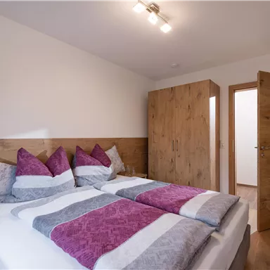 A cozy bedroom with two beds and colorful pillows. The wooden furniture and the bright room create an inviting atmosphere.