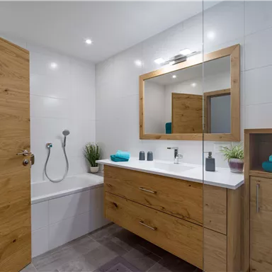 A modern bathroom with a bathtub and a wooden washbasin. The mirror and the plants create an inviting atmosphere.