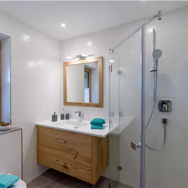 A modern bathroom with a large shower and a wooden washbasin. The walls are brightly tiled and there is a large mirror lighting.