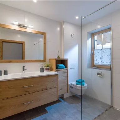 A modern bathroom with wooden details and a glass shower. The space is bright and inviting with blue towels and a large mirror.