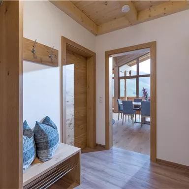 A bright hallway with wood paneling and a sitting area. The dining area is visible through a large window front.