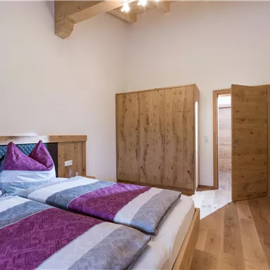 A cozy bedroom with a double bed and colorful cushions. The room has bright walls and wood paneling that create a warm atmosphere.