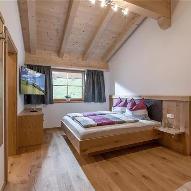 A cozy bedroom with wooden decor and a double bed. Large windows provide plenty of daylight and a beautiful view.