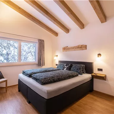 A cozy bedroom with a double bed and wooden ceilings. Through the window, you can see a snow-covered landscape.