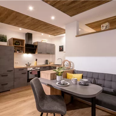 A modern kitchen with wooden shelves and a cozy dining area. The room is bright and inviting with stylish furniture.