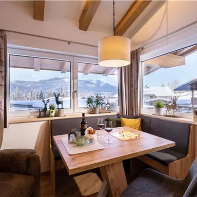 A cozy dining area with wooden chairs and a large table. Through the windows, there is a view of the winter landscape.