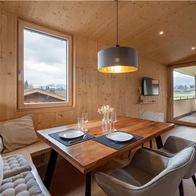 A cozy dining area made of wood with a large table and modern chairs. The room has large windows and offers a view of nature.